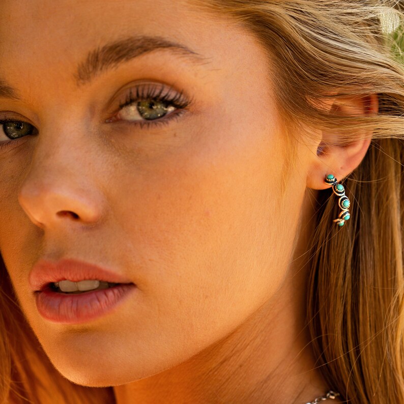 May include: Close-up of a woman's face with a turquoise and silver hoop earring in her right ear.
