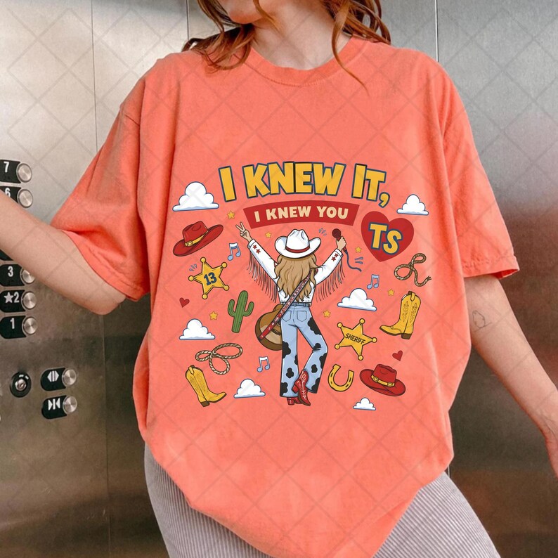 May include: An orange t-shirt featuring a graphic print of a person in a cowboy hat and fringe jacket, blue cow-print pants, and boots. The design includes the text I KNEW IT, I KNEW YOU TS, along with cowboy hats, stars, boots, and cacti.