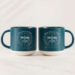 May include: Two teal ceramic mugs with white bottoms. Each mug features the text "BASGIATH WAR COLLEGE" above a crest design. Below the crest is the quote, "There's nowhere in existence you could go that I couldn't find you, Valoria."