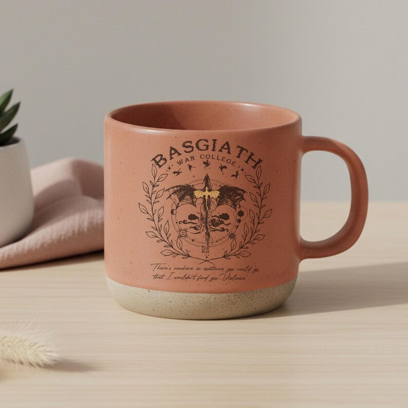 May include: A ceramic mug with a speckled peach exterior and a cream-colored base. The mug features the text "BASGIATH WAR COLLEGE" above a detailed illustration. Below the illustration is the text "There's nowhere in existence you could go that I wouldn't find you - Violence."