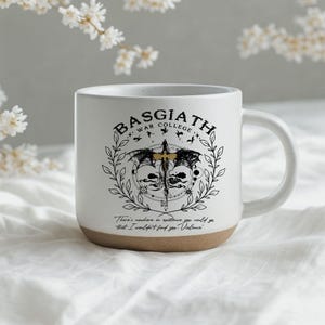 May include: White ceramic mug with a brown base, featuring the text "BASGIATH WAR COLLEGE" and a detailed graphic design. The design includes a sword, wings, and the quote, "There's nowhere in existence you could go that I wouldn't find you. Violence."