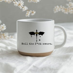 May include: White ceramic mug with a dragon graphic and the text "Well the f*ck aware." The mug has a brown base and a white handle. The dragon graphic is black and gold.