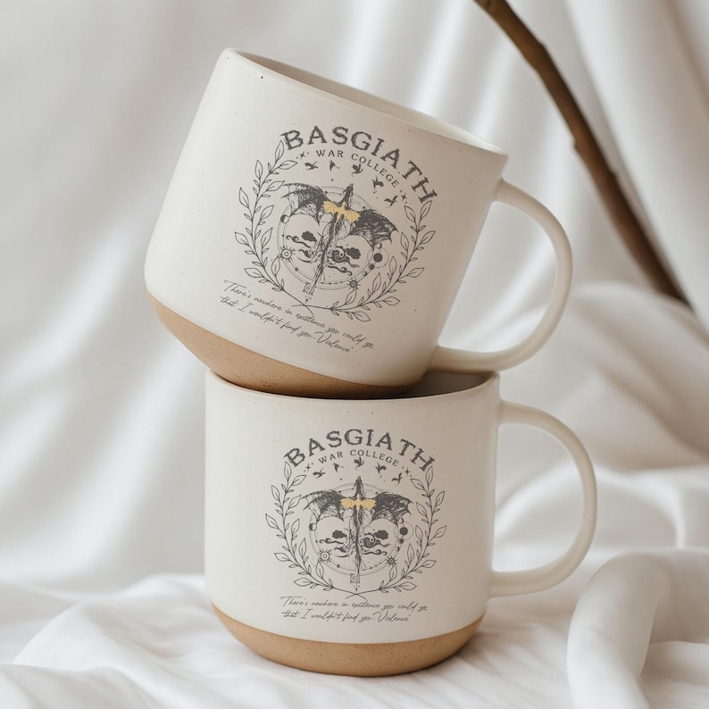 May include: Two white ceramic mugs stacked on top of each other. Each mug has a tan base and a large handle. The mugs feature the text "BASGIATH WAR COLLEGE" above a graphic of a skull, sword, and wings. Below the graphic is the text "There's nowhere in existence you could go that I wouldn't find you, Valens."