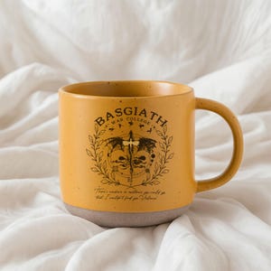 May include: Mustard yellow ceramic mug with a gray base and a large handle. The mug features the text "BASGIATH WAR COLLEGE" above a graphic of a sword and wings. Below the graphic is the text "There's nowhere in existence you could go that I wouldn't find you, Violence."