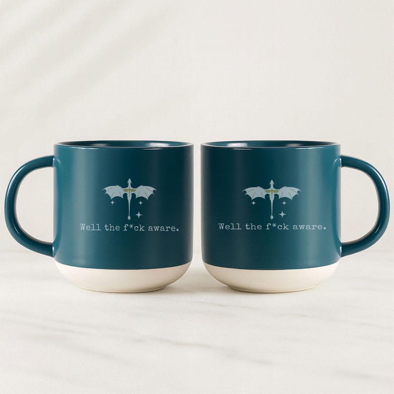 May include: Two teal ceramic mugs with white bottoms and large handles. Each mug features a dragon graphic and the text "Well the f*ck aware." The mugs are identical and sit side-by-side.
