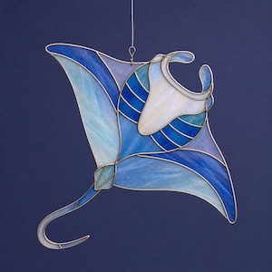 Könnte beinhalten: Eine Glasmalerei-Skulptur einer Mantarochen in Blau- und Weißtönen mit silberfarbenem Metallumriss. Das Kunstwerk weist ein detailliertes Design mit unterschiedlichen Texturen und Mustern auf und schafft ein visuell ansprechendes, aquatisches Thema. Die Skulptur wird von einem dünnen Draht gehalten.