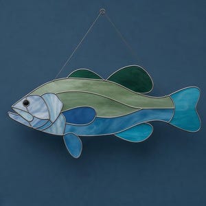 May include: Stained glass fish wall art in shades of blue and green. The fish has a detailed design with a silver metal outline and a wire for hanging. A decorative piece for a nautical or coastal theme.