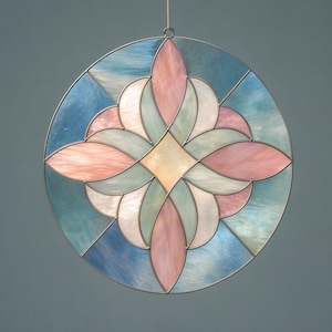 May include: A round stained glass window with a floral design. The window features a central diamond shape in a light yellow color, surrounded by pink, blue, and white petal-like shapes. The glass is framed by a thin metal border and is suspended by a wire.