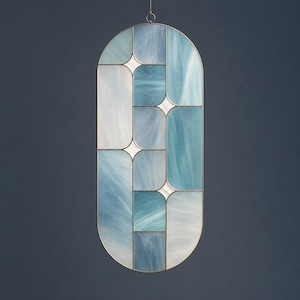 Puede incluir: Una vidriera ovalada con un diseño geométrico. La ventana presenta paneles de vidrio azules y blancos, con un marco metálico. El vidrio tiene un efecto veteado, y el diseño incluye detalles en forma de estrella.
