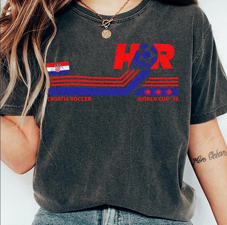 Peut inclure: Un t-shirt gris anthracite orn&eacute; d'un motif avec le texte HR, le drapeau croate et les mots CROATIA SOCCER WORLD CUP '26. Le design comprend des lignes horizontales rouges et bleues ainsi que trois &eacute;toiles rouges, le tout avec un aspect vieilli.