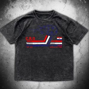 May include: Dark grey t-shirt with a graphic design featuring the letters "C.R.O." in red and white, and a stylized Croatian flag. The design includes the text "EST. 1919" and "WORLD CUP 2023".