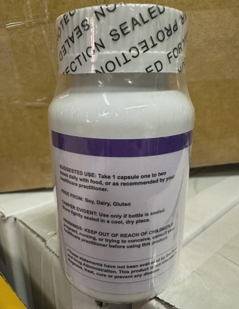 May include: A white supplement bottle with a purple band and clear plastic wrap. The label includes text about suggested use, ingredients, and warnings. The top of the bottle is sealed with a white band that reads "PROTECTION SEALED FOR YOUR".