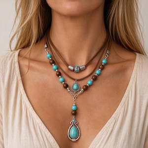 May include: A multi-layered necklace featuring brown suede cords, dark brown wooden beads, and bright turquoise stone beads. The design includes silver-toned metal spacers and a central silver-toned pendant with a teardrop-shaped turquoise stone.