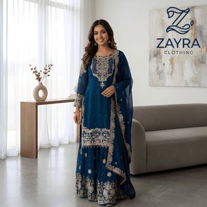 Può includere: Un completo kurta e sharara blu ottanio a maniche lunghe con intricati ricami argentati sul corpetto, sulle maniche e sull'orlo. L'outfit include un dupatta trasparente abbinato con un bordo decorativo, che mostra il logo ZAYRA CLOTHING.