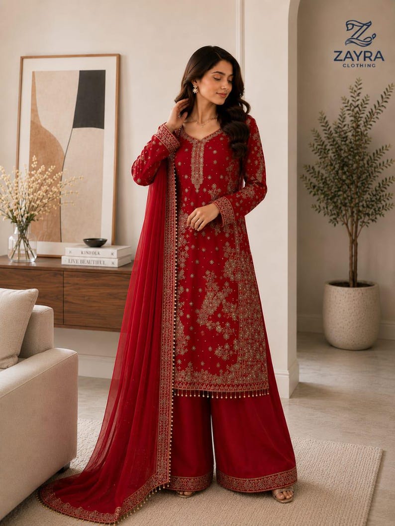 May include: A deep red long-sleeved tunic and wide-leg trousers set featuring intricate gold embroidery throughout the fabric. The ensemble includes a matching sheer red dupatta with a decorative gold border and small hanging beads along the hem.