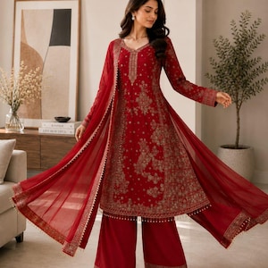 May include: A deep red long-sleeved tunic and wide-leg trousers set featuring intricate gold embroidery throughout the fabric. The ensemble includes a matching sheer red dupatta with a gold-trimmed border and delicate hanging bead details.