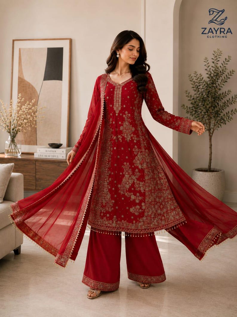 May include: A deep red long-sleeved tunic and wide-leg trousers set featuring intricate gold embroidery throughout the fabric. The ensemble includes a matching sheer red dupatta with a gold-trimmed border and delicate hanging bead details.