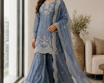 Puede incluir: Un conjunto de tres piezas en color azul polvoriento que incluye una túnica de manga larga, pantalones anchos y una dupatta transparente. Las prendas están adornadas con intrincados bordados plateados y bordes festoneados. Logo Zayra Clothing visible.