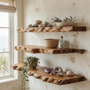 May include: Three horizontal wall-mounted shelves made of natural wood with live edges. The top shelf holds smooth stones and a bowl of greenery. The middle shelf features a woven basket and a glass jar. The bottom shelf displays a trailing plant, amethyst, geode halves, and a sea urchin shell.