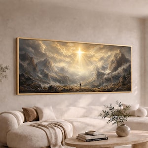 May include: A rectangular landscape wall art piece in a thin gold frame depicting a vast mountain range under a cloudy sky with a bright, central light source shining down. A small, solitary figure stands in the foreground looking toward the peaks.