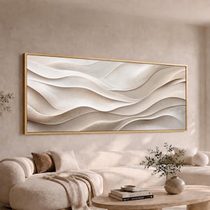 May include: A large rectangular wall art piece featuring a series of flowing, layered, cream and beige abstract waves with a textured appearance, enclosed within a thin, metallic gold frame that highlights the horizontal composition of the artwork.