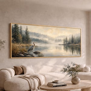 May include: A panoramic landscape painting in a thin gold frame depicting a grey heron standing in shallow water near a rocky shore. The scene features a calm lake surrounded by a dense, misty pine forest under a soft, pale yellow sky.