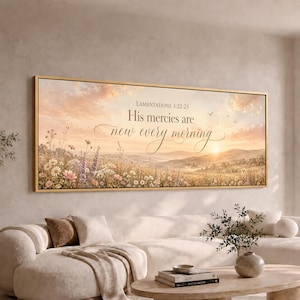 May include: A rectangular wall art print in a gold frame featuring a sunrise over a wildflower meadow. The text reads: LAMENTATIONS 3:22-23 His mercies are new every morning. The scene displays soft pink and orange clouds above rolling hills.