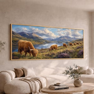 May include: A panoramic landscape wall art print in a gold frame featuring a herd of shaggy brown Highland cattle grazing on a grassy hillside. The scene includes a calm blue lake, rolling green mountains, and a bright sky with white clouds.
