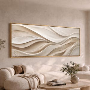 May include: A large rectangular wall art piece featuring abstract, flowing, three-dimensional wave patterns in shades of cream, beige, and off-white. The artwork is encased in a thin, metallic gold frame, displaying a textured, layered surface.