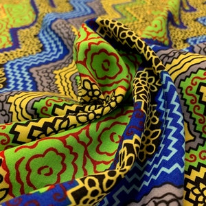 May include: A colorful fabric with a geometric pattern in shades of green, yellow, blue, red, and black. The fabric is folded and draped, showing the intricate details of the design.