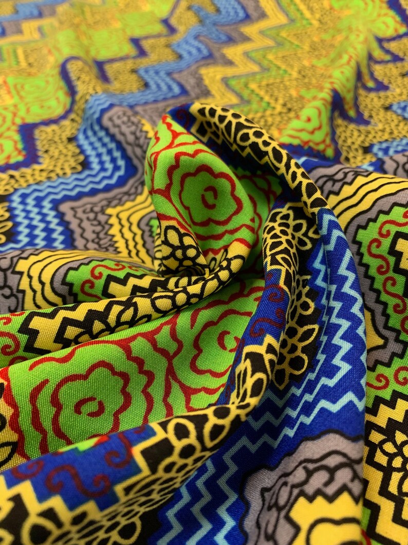 May include: A colorful fabric with a geometric pattern in shades of green, yellow, blue, red, and black. The fabric is folded and draped, showing the intricate details of the design.