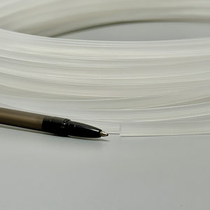 Pu&ograve; includere: Primo piano di un tubo di plastica bianco, arrotolato e posto su una superficie grigia. Una penna nera &egrave; posta accanto al tubo.