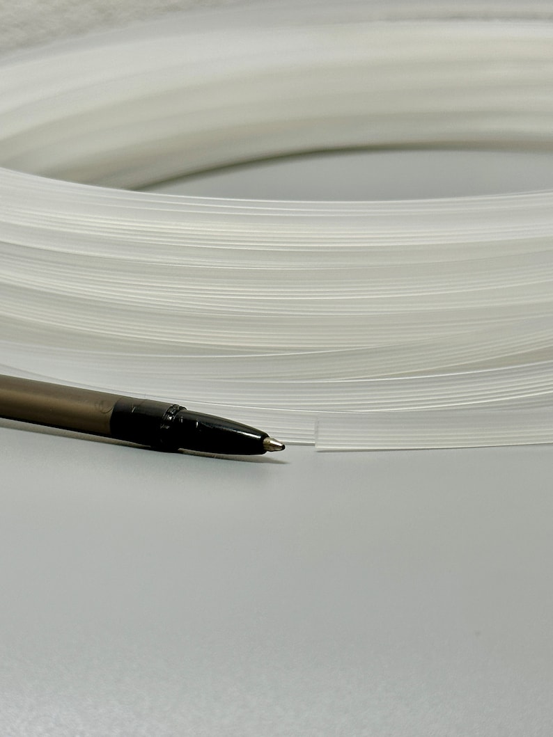 Pu&ograve; includere: Primo piano di un tubo di plastica bianco, arrotolato e posto su una superficie grigia. Una penna nera &egrave; posta accanto al tubo.