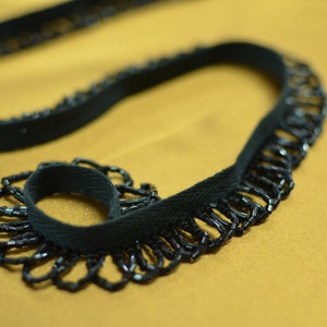 May include: Black beaded trim with a fringe of beads. The trim is made of a black fabric with a black beaded fringe.