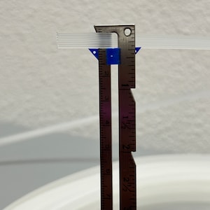 Pu&ograve; includere: Un primo piano di un righello di metallo con un pezzo di plastica blu attaccato ad esso. Il righello &egrave; contrassegnato in pollici e frazioni di pollice. Il righello sta misurando un tubo di plastica trasparente.