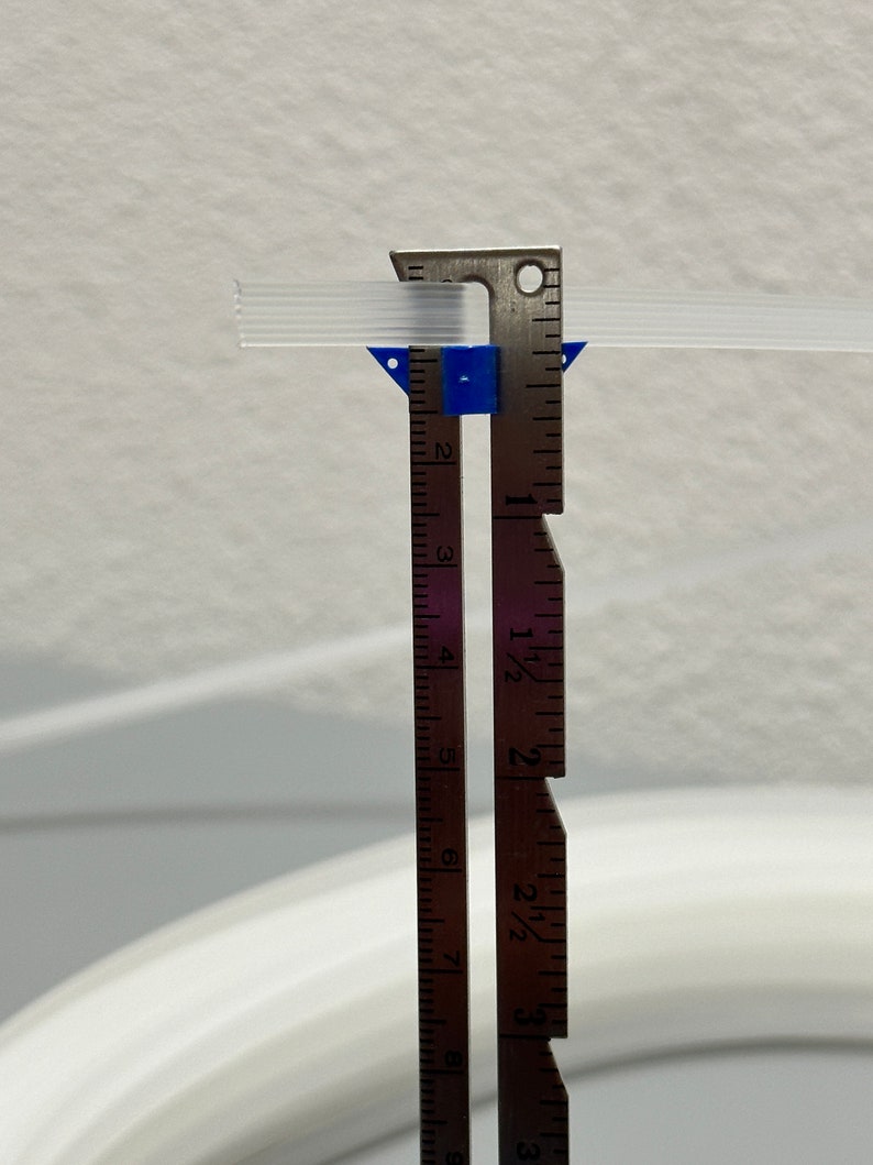Pu&ograve; includere: Un primo piano di un righello di metallo con un pezzo di plastica blu attaccato ad esso. Il righello &egrave; contrassegnato in pollici e frazioni di pollice. Il righello sta misurando un tubo di plastica trasparente.