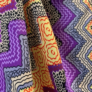 May include: Purple, yellow, and red patterned fabric with a geometric design. The fabric is folded in half, showing both sides of the pattern.