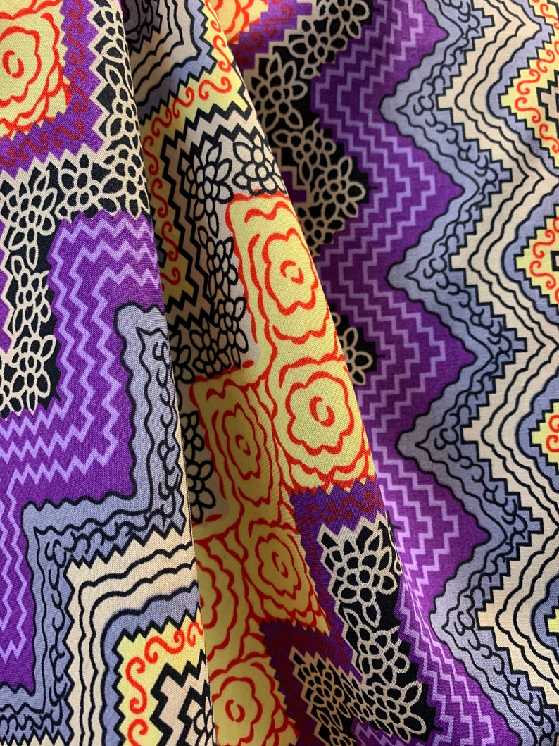 May include: Purple, yellow, and red patterned fabric with a geometric design. The fabric is folded in half, showing both sides of the pattern.