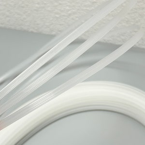 Pu&ograve; includere: Tre cursori per cerniera in plastica bianca, ognuno con una serie di creste parallele, sono disposti in uno schema curvo.