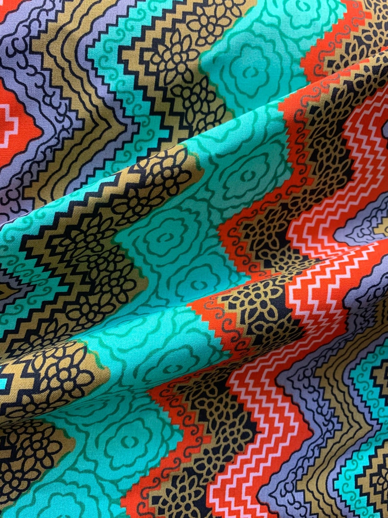 May include: A turquoise, orange, and gold fabric with a geometric pattern. The fabric has a repeating pattern of zigzags, swirls, and floral designs.