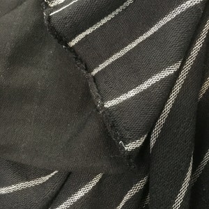 May include: Black and white striped fabric with a white stripe on a black background. The fabric is folded over itself, showing the inside of the fabric.
