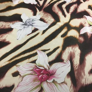 Puede incluir: Una tela beige con estampado de cebra marrón y negro y flores blancas con centros rosas.