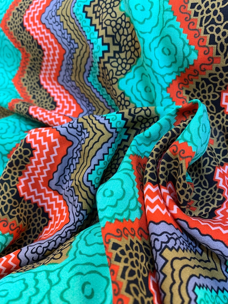 May include: A colorful fabric with a geometric pattern in shades of turquoise, red, black, and gold. The fabric has a wavy, flowing texture.