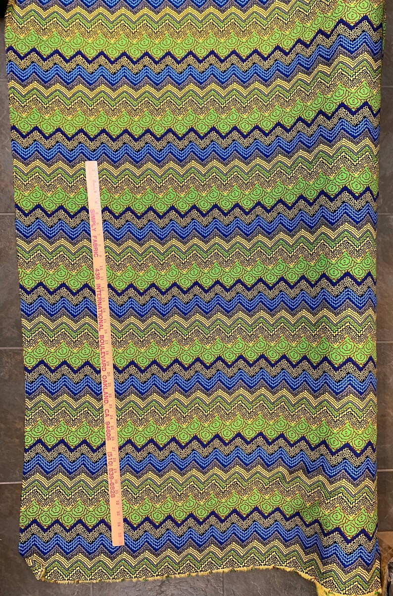 May include: Green, blue, and yellow fabric with a chevron pattern. The fabric is 43 inches wide and has a repeating pattern of small circles.