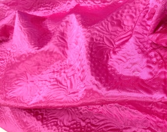May include: A close-up of a pink fabric with a textured, embossed pattern. The fabric is soft and has a slight sheen.