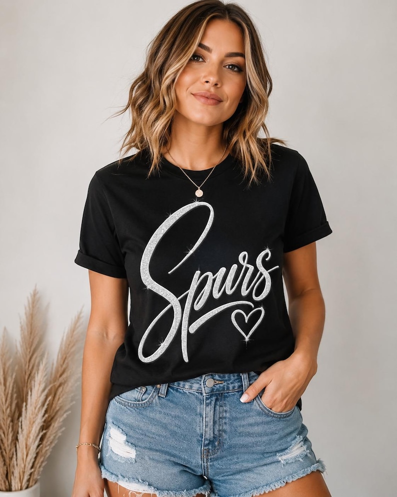 May include: Black t-shirt with the word "Spurs" in a sparkly, cursive font and a small heart below. The shirt is paired with denim shorts. The overall style is casual and comfortable.