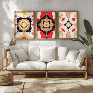 Könnte beinhalten: Drei gerahmte Kunstdrucke mit geometrischen Designs in Rot, Schwarz, Gelb und Creme. Das Kunstwerk hängt über einem weißen Sofa mit großen Kissen. Der Raum hat eine neutrale Farbpalette mit Naturholz und gewebten Texturen.