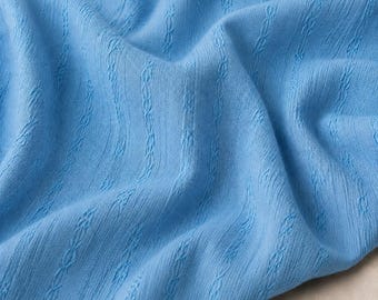 May include: A light blue fabric featuring a vertical textured pattern of repeating cable-like knit columns. The material has a soft, draped appearance with gentle folds that highlight the consistent, repeating woven design across the surface.