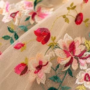 Puede incluir: Una tela de malla beige transparente con intrincados bordados florales. El diseño muestra flores vibrantes en tonos rojos, rosas y blancos, complementadas con tallos y hojas verdes, creando un patrón botánico detallado en el tejido.