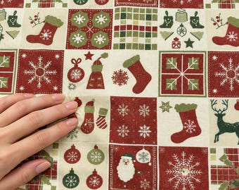 Op de afbeelding: Een stof met een ruitpatroon van kerstvierkanten in rood, groen en crème. Het ontwerp bevat illustraties van de Kerstman, kerstsokken, sneeuwvlokken, rendieren, kerstballen en hulstbladeren gerangschikt in herhalende blokken.